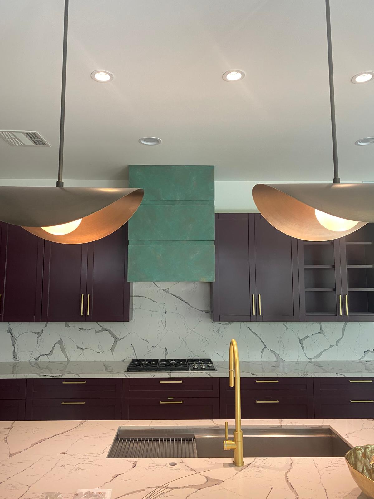 Kitchen with plum cabinets, patina green hood, marble backsplash and sculptural brass pendants, Montrose