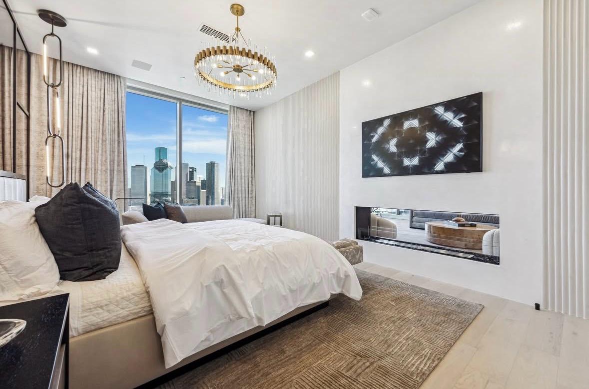 Primary suite fireplace, gold chandelier and Houston skyline, The Residences at The Allen